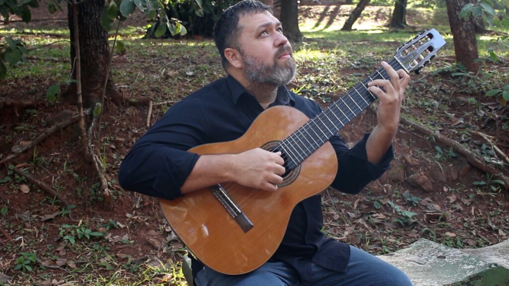 2a foto de Henrique Candido Toando Violão de 7 cordas sentado em uma praça e olhando para cima
