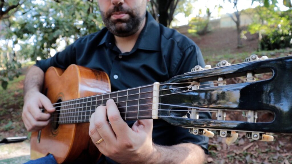 1a foto de Guilherme Mauad tocando violão 6 cordas sentado em uma praça